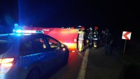 Wypadek drogowy, czerwony parawan rozstawiają funkcjonariusze Straży Pożarnej, z przody stoi radiowóz policyjny