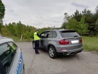 Policjant Ruchu Drogowego kontroluje samochód, z boku stoi radiowóz oznakowany