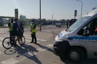 policjanci z ruchu drogowego kontrolują rowerzystę, obok stoi radiowóz oznakowany, oraz redaktorzy z lokalnych mediów