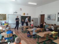 klasa szkolna, przy tablicy stoi policjantka i pracownik WORD w Skierniewicach, który zakłada na rękę uczniowi opaskę odblaskową