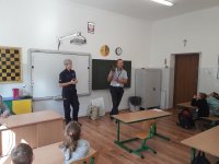 klasa szkolna, przy tablicy stoi policjantka oraz pracownik WORD w Skierniewicach, który pokazuje sygnalizator świetlny uczniom. Uczniowie siedzą w ławkach