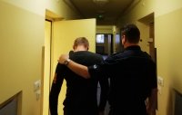 policjant konwojuje podejrzanego o włamania do policyjnego pomieszczenia dla zatrzymanych