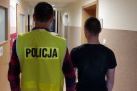 korytarz w Komendzie Powiatowej Policji w Kutnie policjant ma założona kamizelke odblaskowa z napisem Policja, prowadzi zatrzymanego