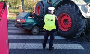 droga wypadek samochodowe, samochód osobowy znajduje się częściowo pod kołami ciągnika rolniczego. Przed pojazdami stoi policjant