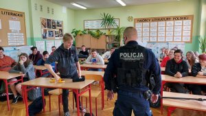 klasa szkolna policjant stoi tyłem do klasy, w ławkach siedzą uczniowie