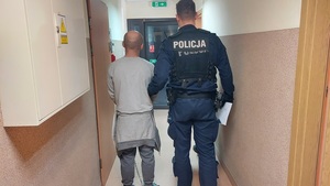 policjant prowadzi zatrzymanego mężczyznę korytarzem komendy.