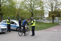 Policjanci kontrolują rowerzystę, w tle radiowozy oznakowane