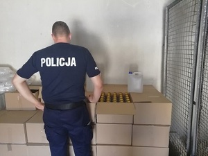 w tle butelki plastikowe w kartonach obok policjant stojący tyłem