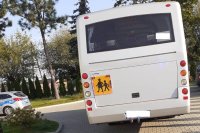 autobus szkolny z tyłu na parkingu, po lewej stronie widać kawałek radiowozu oznakowanego