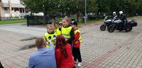 Dwie dziewczynki na placu przed szkolą podstawową udzielają wywiadu, przed nimi redaktorzy trzymający mikrofony, w tle stoją motocykle policyjne
