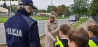 dziecko wręcza opaskę odblaskową kobiecie na ulicy, obok policjantka