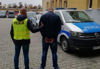 policjant w kamizelce odblaskowej prowadzi do radiowozu zatrzymanego