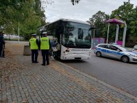 policjanci z Ruchu Drogowego stoją przed autokarem, pasażerka wchodzi do autokaru. Autokar stoi na przestanku autobusowym