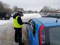 policjant stoi przy samochodzie od strony kierowcy, pokazuje kierowcy ulotkę