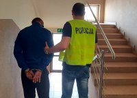 korytarz w jednostce, po prawej stronie schody, policjant sprowadza zatrzymanego w dół po schodach, zatrzymany ma założone kajdanki na ręce trzymane z tyłu.