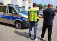 dziedzinie jednostki, policjant prowadzi zatrzymanego do radiowozu, z lewej strony widać radiowóz