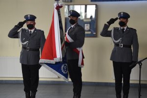 sztandar policji stoi na sali odpraw dwóch policjantów salutuje