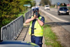 policjant stoi na drodze i mierzy prędkość urządzeniem ,