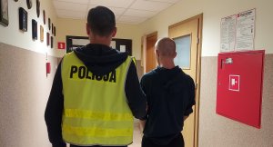 policjant w kamizelce odblaskowej z napisem policja prowadzi zatrzymanego korytarzem