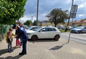 chodnik przed jedną ze szkół podstawowych, policjantka rozdaje dzieciom odblaski, rodzice prowadzą dzieci ze szkoły