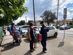 chodnik przed jedną ze szkół podstawowych, policjantka rozdaje dzieciom odblaski, rodzice prowadzą dzieci ze szkoły