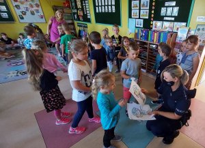 policjantka w przedszkolu, dzieci stoją dookoła, dziewczynka wręcza policjantce rysunek