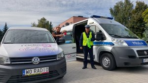 parking, na parkingu zaparkowany radiowóz policyjny oraz samochód z radia q, przy nich stoją redaktor i policjant