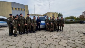 dziedziniec jednostki, radiowóz policyjny na sygnałach, uczniowie stoją obok radiowozu