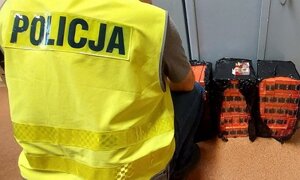 paczki papierosów leżą przy szafie pancernej obok kuca policjant w kamizelce odblaskowej z napisem Policja