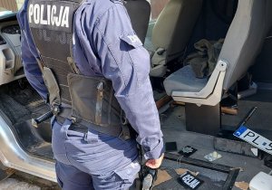 Policjant stoi przed samochodem, na podłodze samochodu leżą łom, legitymacje policyjne emblemat z napisem służba celna