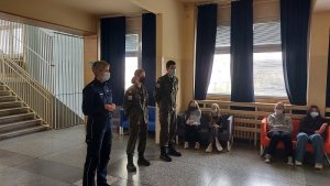 szkoła podstawowa nr 1 w kutnie, sala widowiskowa na kanapach siedzą dzieci, policjantka i dwóch uczniów ze szkoły mundurowej prowadza prelekcję