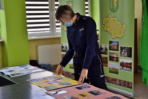 sala, na stole leżą prace plastyczne, policjantka ogląda prace.