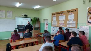 klasa szkolna policjant stoi przodem do klasy, w ławkach siedzą uczniowie