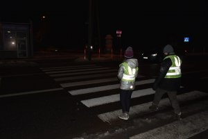 Dzieci przechodzą przez przejście dla pieszych w kamizelkach odblaskowych , na plecach odblaskowe skrzydła anioła