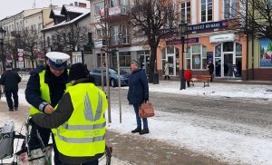 policjant z Ruchu Drogowego rozdaje kamizelki odblaskowe, pani z rowerem zakłada kamizelkę obok mieszkańcy