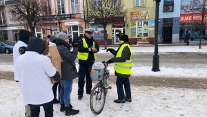 policjant z Ruchu Drogowego rozdaje kamizelki odblaskowe, pani z rowerem zakłada kamizelkę obok mieszkańcy