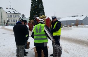 plac wolności w Kutnie ,policjant z ruchu drogowego rozdaje kamizelkę obok stoi mieszkaniec z założoną kamizelką i pracownicy fundacji