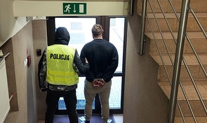 policjant z kamizelce odblaskowej z napisem Policja prowadzi zatrzymanego, klatka schodowa