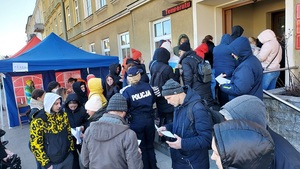 policjanta stoi przed urzędem miasta i rozdaje uchodźcom ulotki , przed budynkiem tłum ludzi.