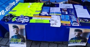 na stole leżą broszury i ulotki na dole wiszą plakaty