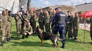 policjant stoi z psem służbowym , obok uczniowie szkoły mundurowej