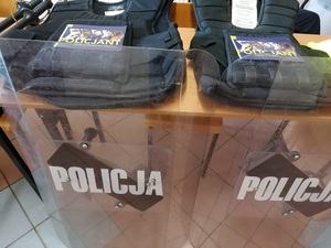 tarcze z napisem Policja stoją oparte o stół na stole leżą kamizelki taktyczne na nich ulotka z napisem Policja