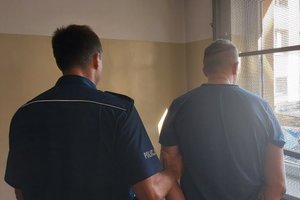 policjant trzyma za rękę zatrzymanego po prawej stronie krata