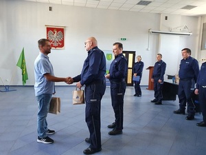 Komendant Powiatowy Policji w Kutnie wręcza upominek mieszkańcowi, ściska mu dłoń, za komendantem stoi policjant.