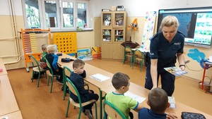 klasa, dzieci siedzą w ławkach policjantka rozdaje plany lekcji