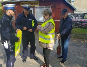 dwóch policjantów stoi na chodniku pani zapina kamizelkę odblaskową obok stoi pan