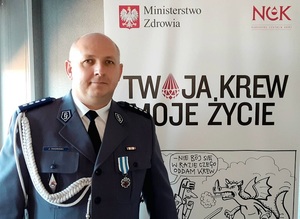 policjant stoi w mundurze obok ścianka obok napis Twoja krew Moje życie