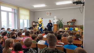 klasa dzieci siedzą na krzesłach z przodu pani policjantka i pluszowa maskotka mrówka