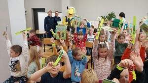 zdjęcie grupowe, dzieci trzymają w rękach książeczki i odblaski z tył€ stoją policjantki i pluszowa maskotka mrówka