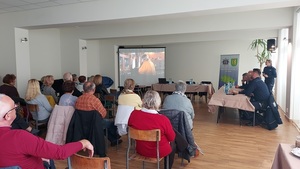 sala konferencyjna seniorzy siedzą na krzesłach z przodu policjanci stoją przy stole